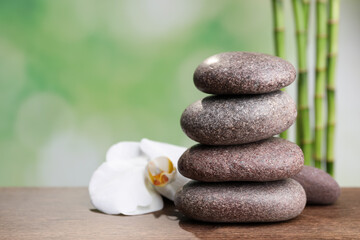 Stacked spa stones and orchid flower on wooden table against bamboo stems. Space for text