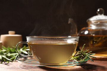Cup of aromatic herbal tea and fresh rosemary on wooden table