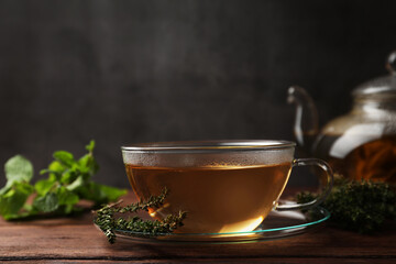 Cup of aromatic herbal tea and fresh thyme on wooden table