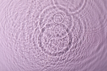 Clear water with rippled surface on pink background, top view