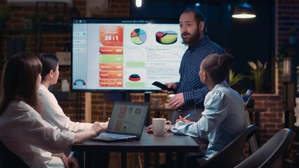 Company executive presenting analytics research in business meeting, showing statistics on screen. Employee marketing report presentation, diverse team planning sales strategy - Powered by Adobe