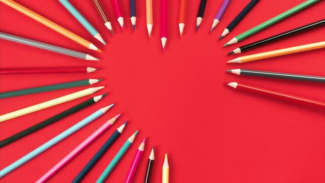 Composition of colorful pencils appearing one by one to make heart shape on red back view. Saint Valentines and love greeting for holidays. Handwriting card and congratulation. Stop motion, copy space