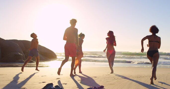 Friends, summer and beach vacation with friends running to water with energy, fun and happiness in bikini and swimwear at sunset. Group of social men and women together on holiday at sea for freedom