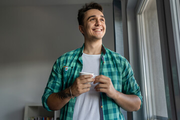 Man standing by the window with cup of coffee in morning daily routine