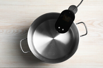 Thermal immersion circulator in pot on white wooden table, top view. Sous vide cooker