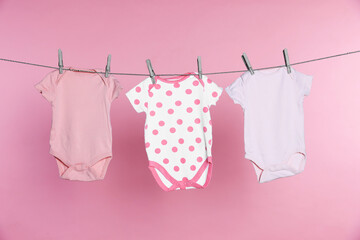 Baby onesies drying on laundry line against pink background