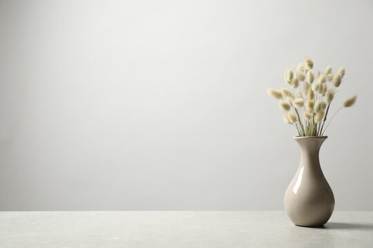 Dried flowers in vase on table against light background. Space for text