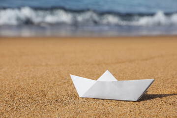 Fototapeta na wymiar White paper boat near sea on sandy beach, space for text