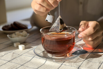 Woman taking tea bag out of cup at table indoors, closeup