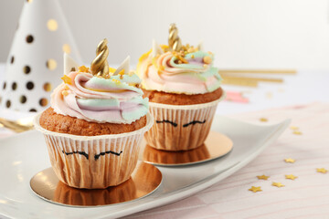 Plate with cute sweet unicorn cupcakes on white table, closeup. Space for text