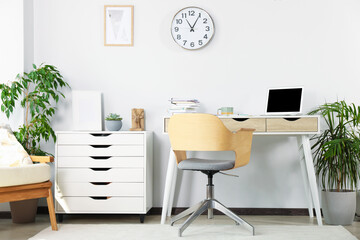 Beautiful workplace with laptop on white wooden table, chair and houseplants in room