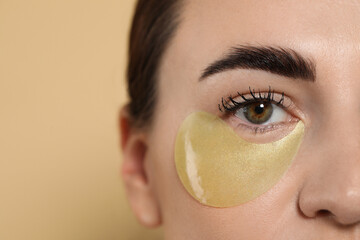 Beautiful woman with under eye patch on beige background, closeup. Space for text