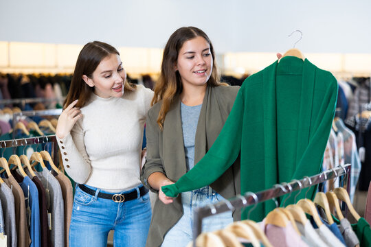 Two young cheerful women shopping in outerwear clothing boutique