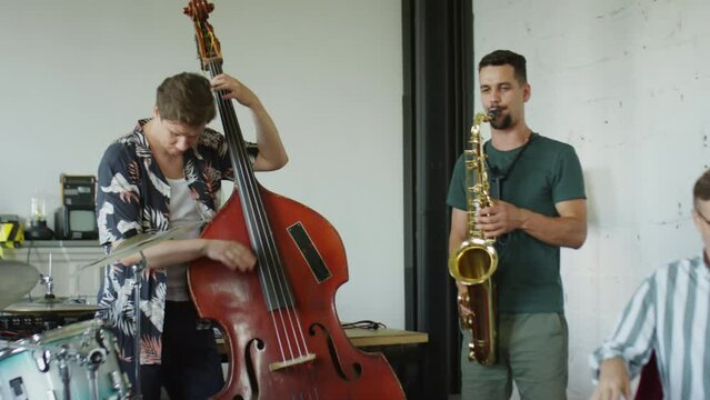 PAN shot of jazz musicians playing saxophone, synthesizer, double bass and drum set in studio