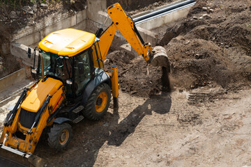 An excavator digs the earth with a bucket at a construction site.