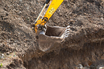 Excavator bucket close-up against the background of a dug pit