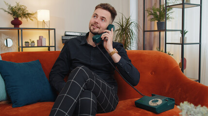 Portrait of man making wired telephone conversation with friends sitting call on couch at home...