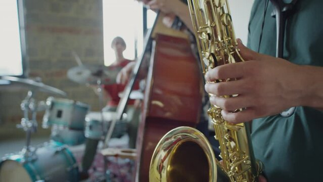 Selective focus shot of jazzman playing saxophone on rehearsal with music band in studio