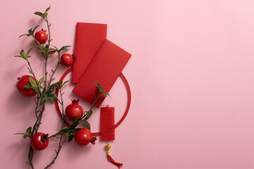 Chinese lunar new year background with empty space. Red pomegranate branch, lucky envelopes, and lucky ornaments on pink background. New year Title presentation.