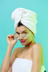 Vertical photo, a woman on a blue background in a towel on her head and body and glasses looks at us