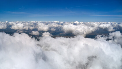 Aerial view from airplane window at high altitude of earth covered with puffy cumulus clouds forming before rainstorm
