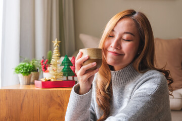 Portrait image of a young woman in sweater drinking hot coffee with Christmas holiday decoration at home