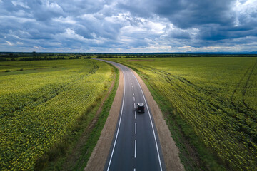 Aerial view of intercity road between green agricultural fields with fast driving car. Top view from drone of highway traffic