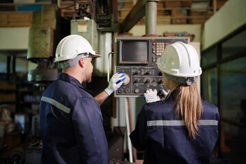 Young successful technician or repairman of industrial machines in safety helmet and workwear standing in large garage or workshop