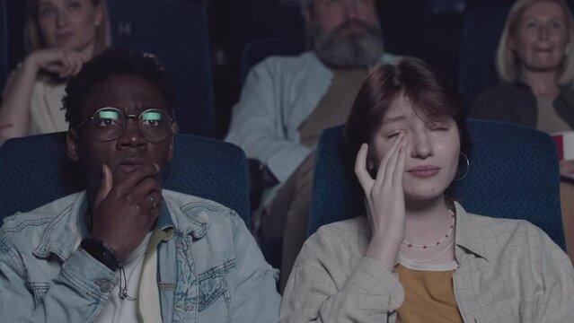 Young African American man and his Caucasian girlfriend crying when watching heartbreaking drama movie in cinema