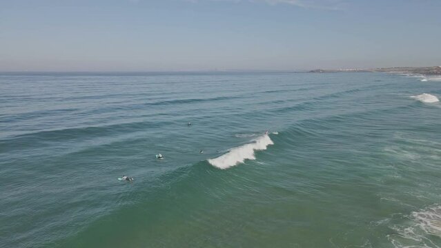 Aerial view of surfers in Alentejo, Portugal. Drone flying forwards over fit people surfing.