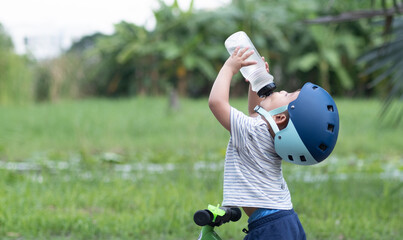Cute Baby boy on a bike wearing helmet drinks water from water bottle