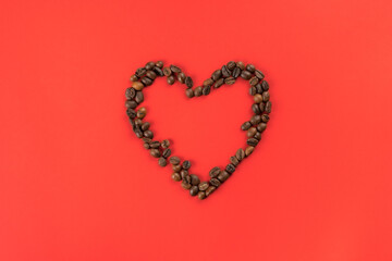 Brown coffee beans forming heart contour on red studio background. Charity and donation on holidays. Falling in love and confession on saint valentines day. I give you my heart. Flat lay, copy space