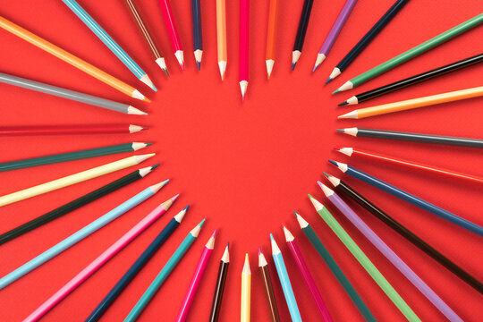 Composition of colorful pencils forming heart shape by slate pencils on red studio background. Saint Valentines love and wedding greeting card for romantic holiday party event. Flat lay, copy space