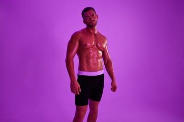 Man athletic body bodybuilder in briefs with nude torso abs full-length in the background fitness classes, purple colored light. Advertising, sports, active lifestyle, competition, challenge concept. 