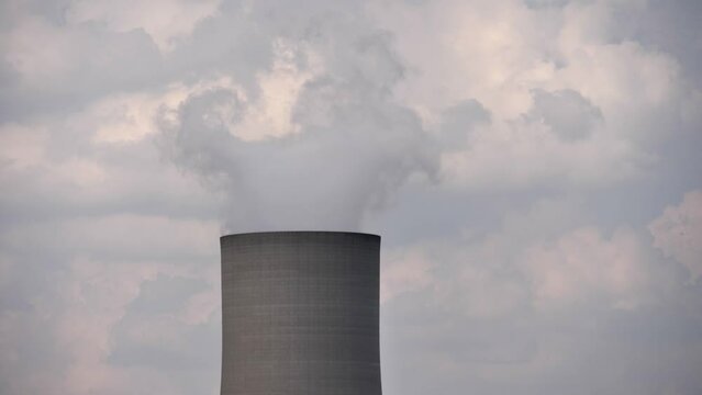 Steam rises from lone industrial cooling tower chimney into cloudy sky