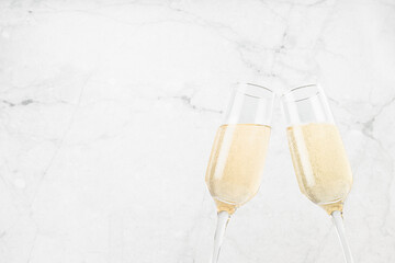Christmas festive background with two sparkling champagne wine glass in knock motion as toast and congratulations on modern white marble backdrop, copy space, closeup. Holiday beverage for party.