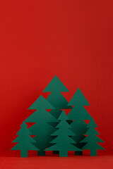 Christmas festive background in traditional red and green color with green paper spruces in minimal cartoon style, copy space, vertical. New year mockup for presentation, design, card, poster, flyer.