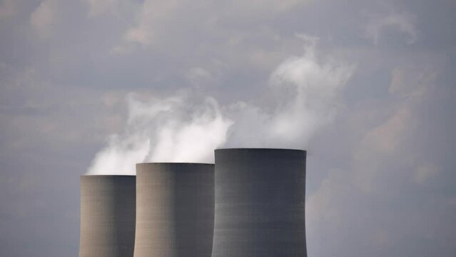 Steam rises into cloudy sky from cooling towers at power plant station