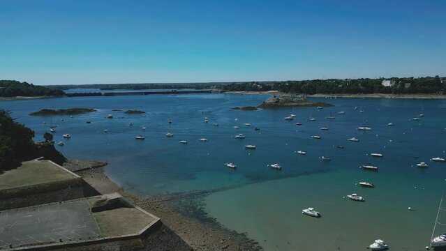 Drone flying over boats moored on bay of Solidor beach with Rance Dam in background, Brittany in France. Aerial forward. Blue sky for copy space