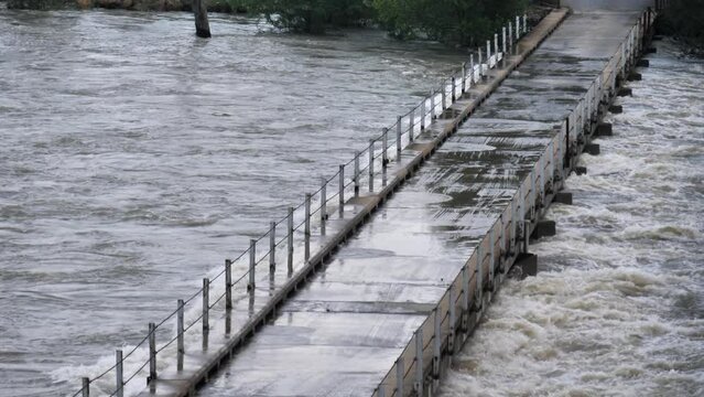 Low single lane bridge across flooding river has water up to the deck
