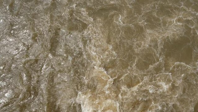 High angle view of muddy brown fast flowing river water rushing past