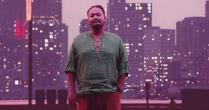 Portrait of a young pacific islander businessman in casual clothes or hipster looking at the camera. Plus size entrepreneur or manager posing, cityy in the night in background. 