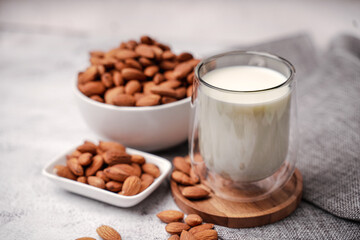 Glass of almond milk with almond seed on white concrete background.