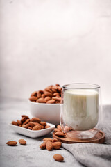 Glass of almond milk with almond seed on white concrete background.