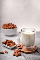 Glass of almond milk with almond seed on white concrete background.