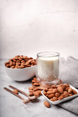 Glass of almond milk with almond seed on white concrete background.