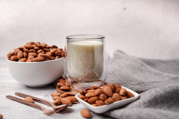 Glass of almond milk with almond seed on white concrete background.