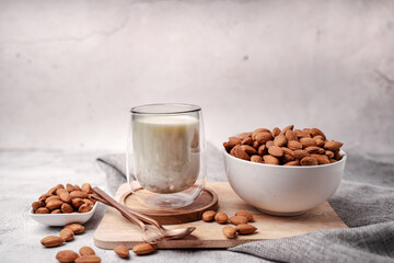 Glass of almond milk with almond seed on white concrete background.