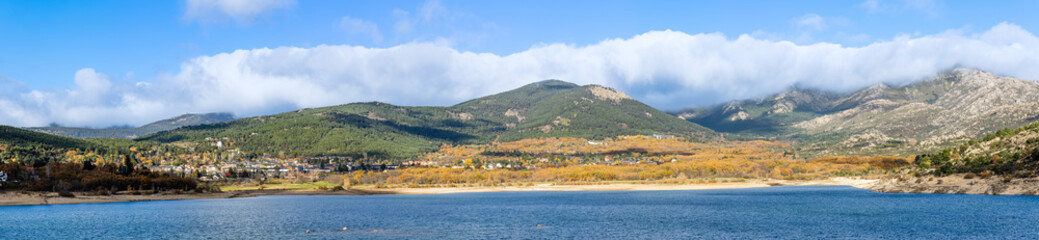 Fototapeta na wymiar Navacerrada reservoir in autumn with the town in the background and the mountains of the Sierra de Guadarrama in Madrid