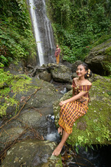 Portrait of two girls in front of a waterfall in a tropical forest, dressed in a traditional sarong